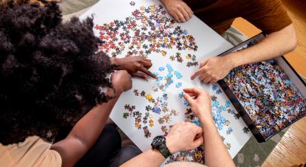 A high level view of three adults working together to complete a puzzle.