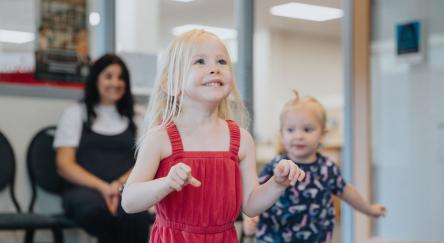 Two toddler girls try to catch bubbles at Toddler Time while their parent watches in the background.
