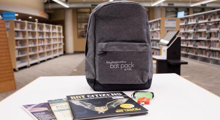 An FVRL Bat Pack sits on a table in the library. The kit includes a backpack with a bat detector and information about bats. 