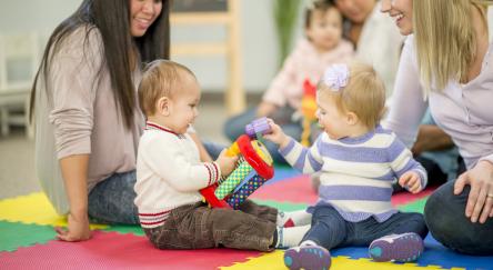 A multi-ethnic group of babies and their mothers playing together with toys in a group setting.