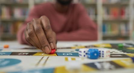 A young African American Man (20s) plays a board game on a table in the library.