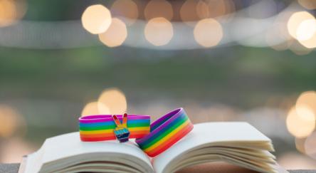 Rainbow wristband celebrating lgbtqia+ groups sit atop a library book with a defocused background.
