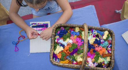 Child girl learning to use cardboard weaving loom.