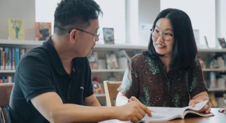 A man and a woman are sitting together at Maple Ridge Public Library. An open book sits on the table.