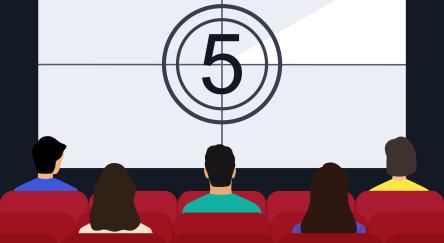 Movie theater interior with people sitting on red seats in front of movie screen.