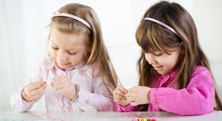 Two little girls making beaded friendship bracelets. 
