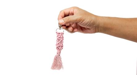 Hand is holding a pink macrame keychain on a white background.