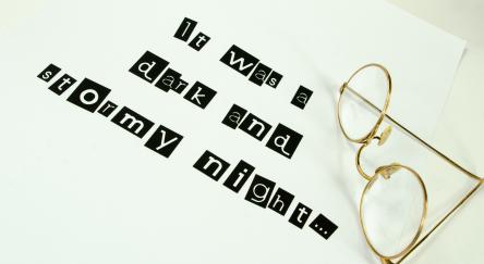 A pair of vintage gold framed glasses isolated on a sheet of paper with the saying- It was a dark and stormy night.