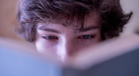 Close up view of a Caucasian brown haired man's (18) brown eyes looking in a book with a blue cover.