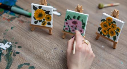A hand paints beautifully handpainted artwork on small canvases, displaying vibrant floral designs on artist easels.
