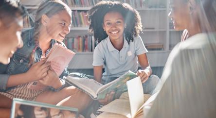 A diverse group of tweens sitting on the library floor, engaged in an animated discussion about the books they are reading.