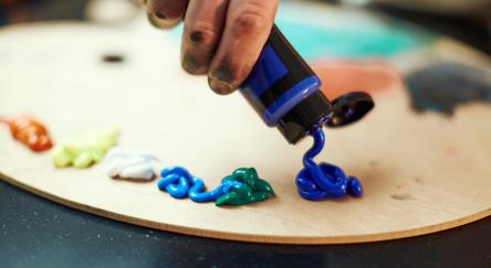 Close-up painter hand squeeze acrylic blue paint from tube on wooden painting palette.