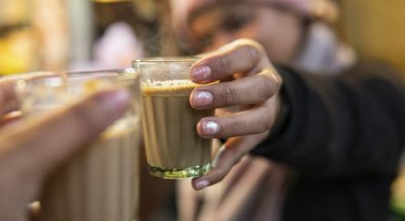 Close up image of a woman’s hand holding a transparent cup of chai.