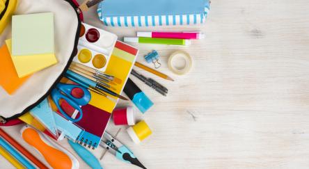 Various craft supplies spilling out of backpack onto grey table.