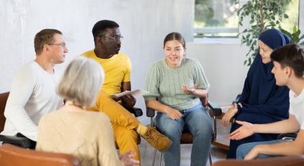 A diverse group of people engaged in conversation while seated in a circle in a well-lit room.