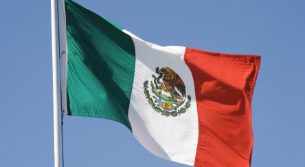 Horizontal view of a Mexican national flag waving in the wind against a clear blue sky.