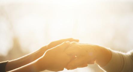 Two hands grip each, one young - one old, with the sun setting in the background.