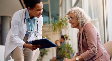Smiling senior woman and her doctor going through paperwork in hallway at medical clinic.