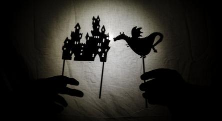 Shadow theater for children projected on a bed sheet. The shadows are of cardboard with a little basset, you can also see the hand that manipulates them. tales, the fairy, storyteller.