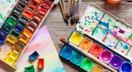 Set of watercolor paints, brushes for painting and paper sheet of painting on old wooden background. 