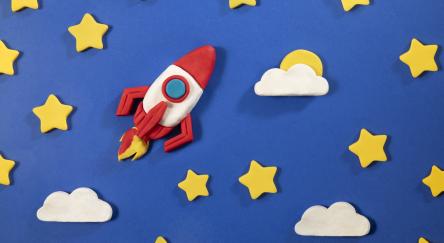 Space rocket and stars made with play clay on blue background.