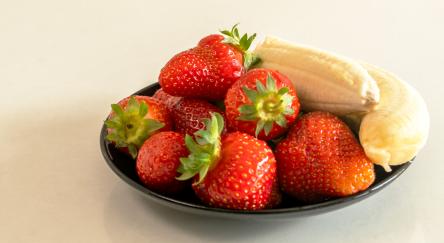 Strawberries and bananas are in a bowl on a table.