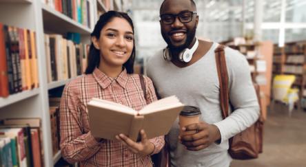 A young woman and a young man are looking for books in a library.