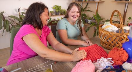 Two adult women collaborate on knitting a beautiful bag.