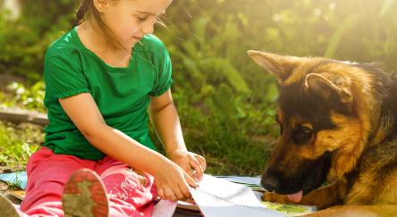 Young girl reading to a German Shepard dog outside on a mat.