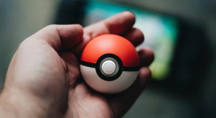A pale hand holds a Poké-ball.