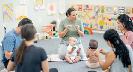 A small group of parents and their babies, participate in a sign language class together.