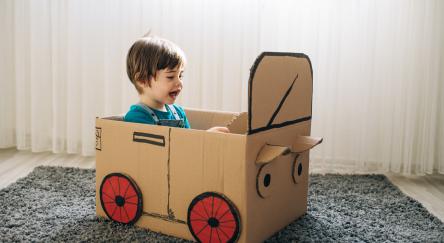 Little boy plays in the cardboard car.