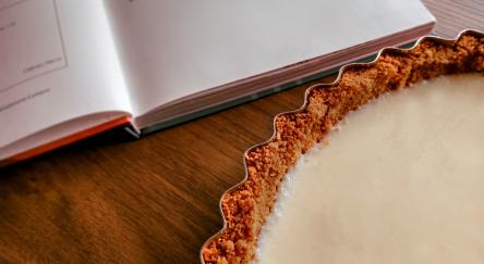 A freshly baked tart lays on a table by an open cookbook.