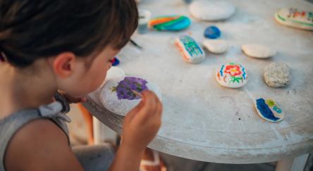 Little girl paints rocks using different colors.