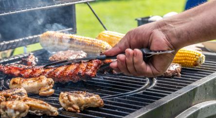 Close-up of man using tongs to take meat off on hot barbecue grill.