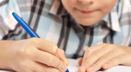 Young boy doing his homework with a blue pen.
