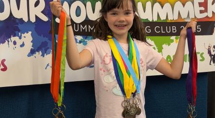 A smiling girl holds up bundles of Summer Reading Club medals.