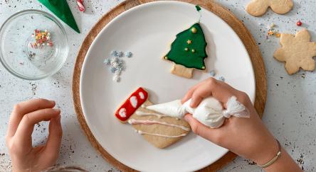 Table top view of teen girl hands decorating homemade Christmas cookies.