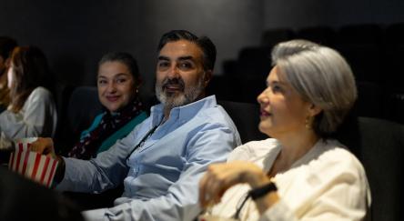 People enjoying popcorn while watching a movie in a cozy cinema, sharing smiles and laughter in a lively atmosphere.