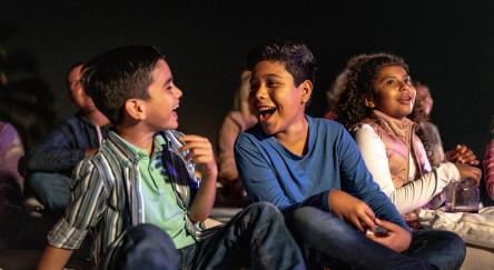 Young kids sitting on the library floor, joking around, and enjoying a movie.
