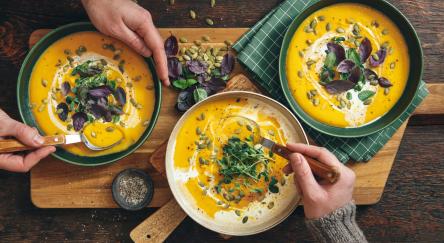 Men eating Vegan Creamy Roasted Pumpkin Soup on wooden background.
