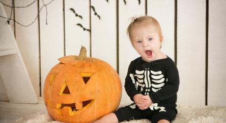 Little girl sitting dressed as a skeleton sitting near a jack-o-lantern pumpkin.