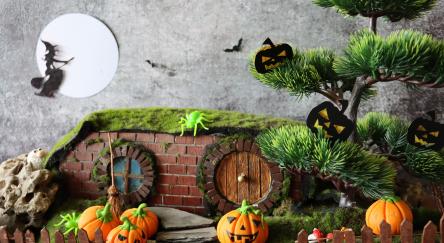 A Halloween diorama night scene with witch flying on broom across full moon, jack-o-lanterns, and bats.