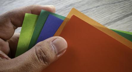 Hand holding a fan of colorful origami paper sheets, a vibrant craft project.