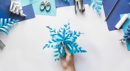 Top down view of hands making three dimensional paper snowflake decorations.