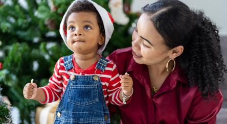 Mother and toddler son play together near Christmas tree.