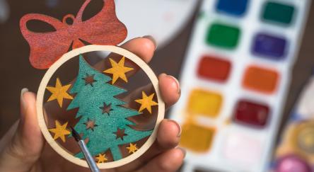 Person paints a wooden ornament to hang on a tree.