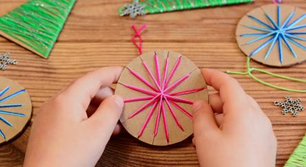 Child's hands making yarn wrapped cardboard Christmas ornaments.