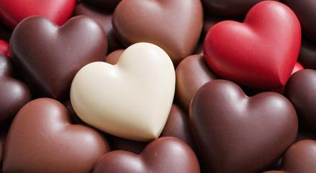 An assortment of heart-shaped chocolates in various colors, including dark, milk, white, and red chocolate.