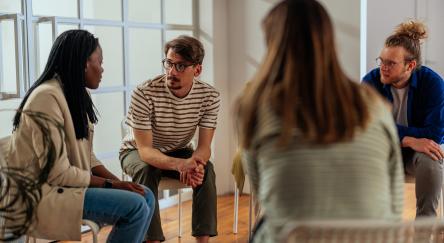 Group of people sitting on chairs in a circle and discussing things together.